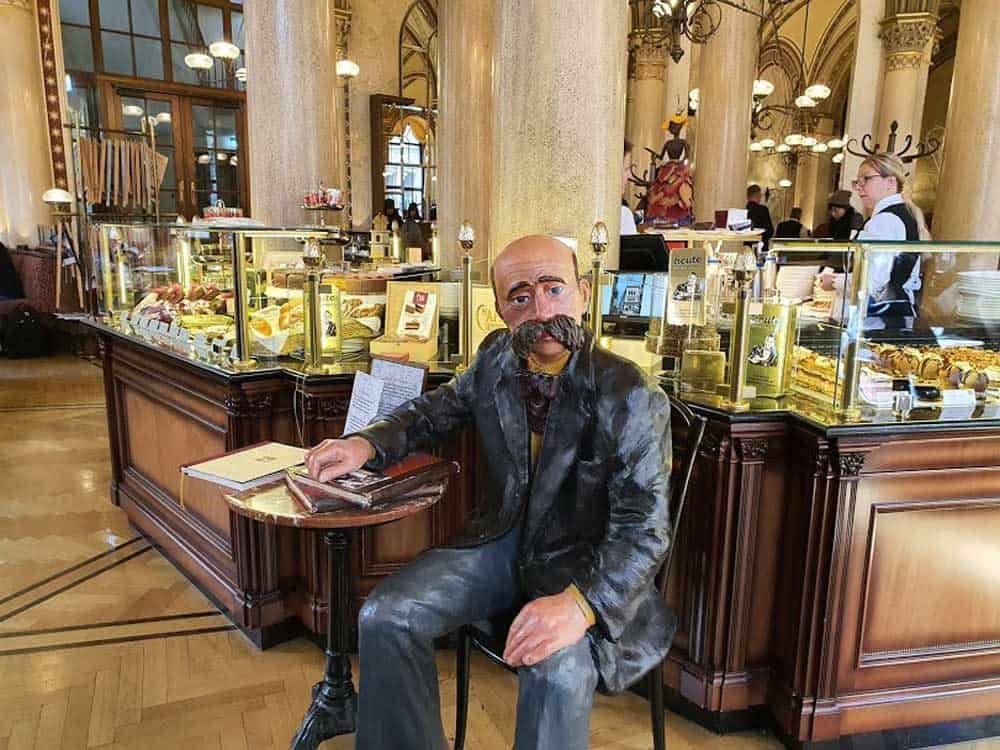 Statue of a man sitting at a table inside a Vienna cafe.