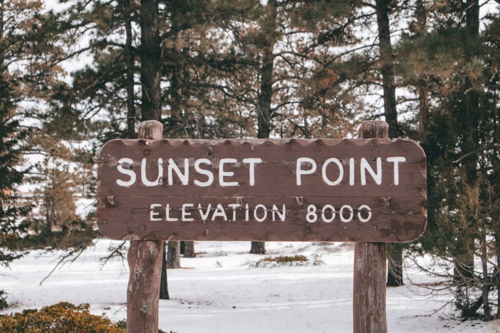 Trail sign says Sunset Point surrounded by snow.