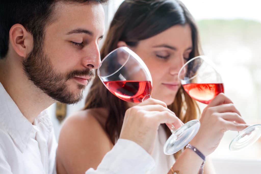 Two people holding wine glasses up to their nose and sniffing it.