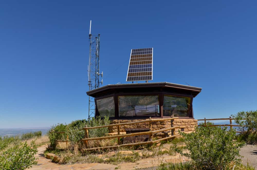 small outpost building at the top of a mountain with a circular walkway around it 