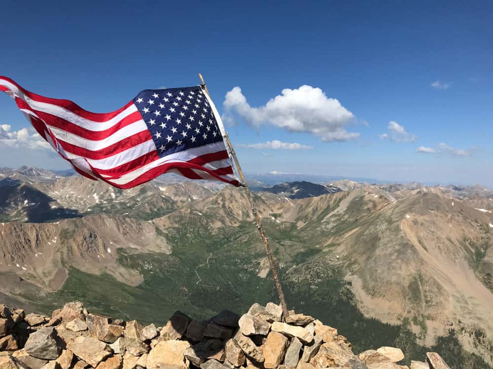 American flag tied to a large stick placed at the top of a mountain peak 
