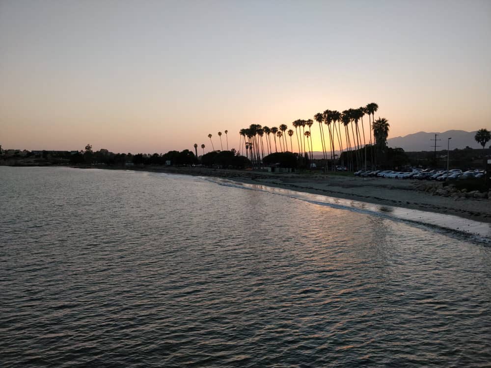 view of the sun at sunset shinning through palm trees on the water