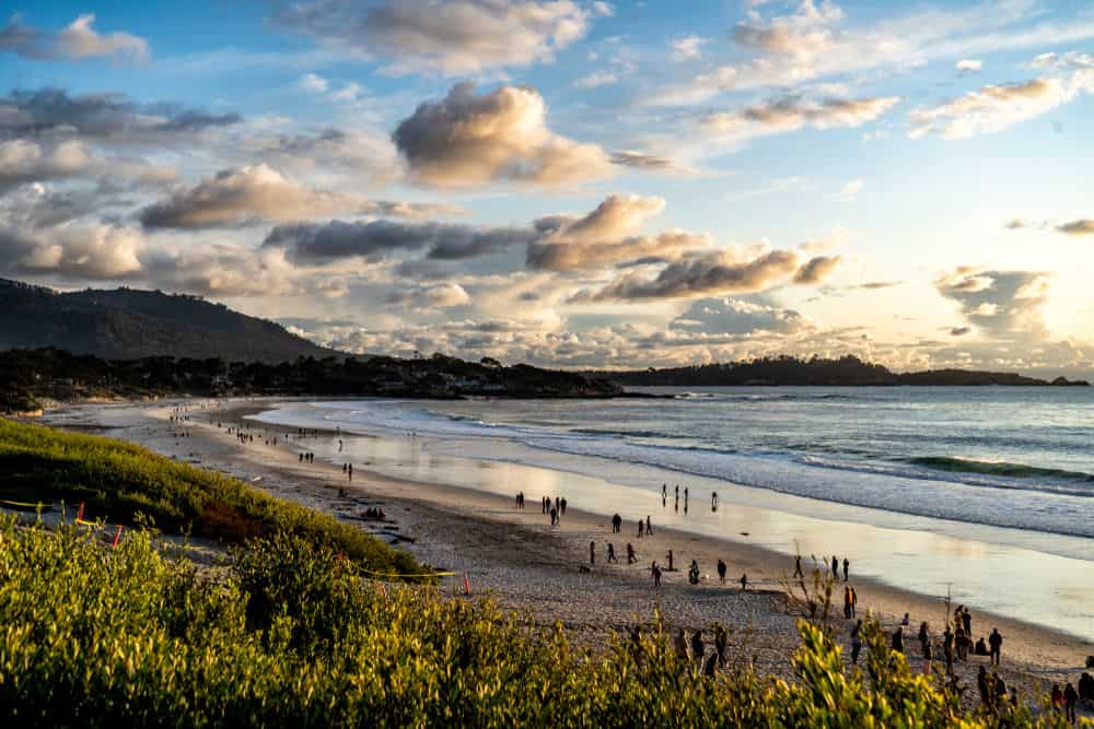 people walking along the edge of the water on a beach at sunset