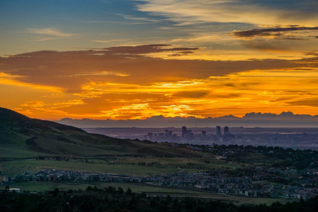 Orange sky at sunset over a city skyline by mountains.