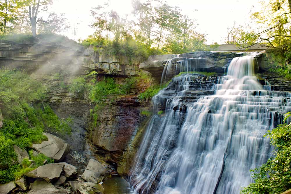 Water cascades down a rocky cliff into a pool of water.
