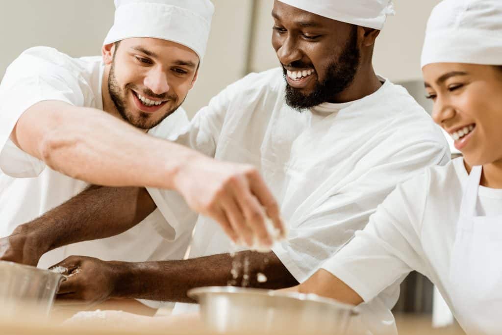 Three chefs in a kitchen sprinkling flowers into bowls. 