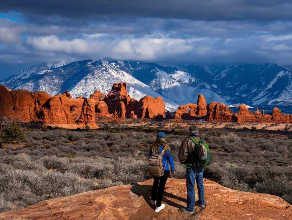 Two hikers standing in the desert with a big mountain covered in snow behind.