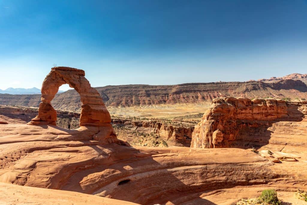 Person standing under an arched rock in a desert landscape.
