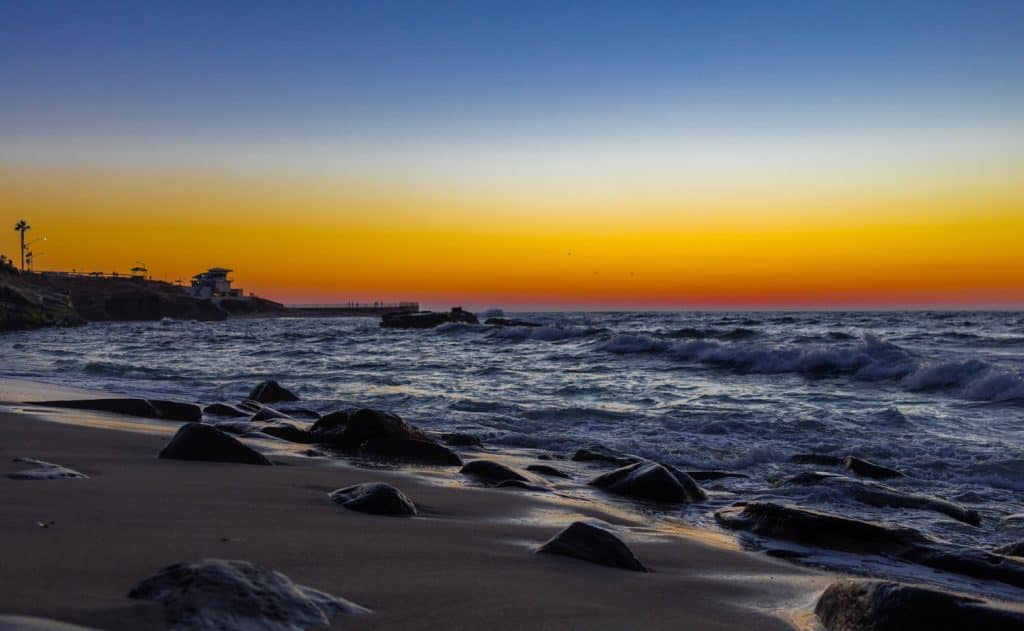 Orange and blue sky over a rocky beach.