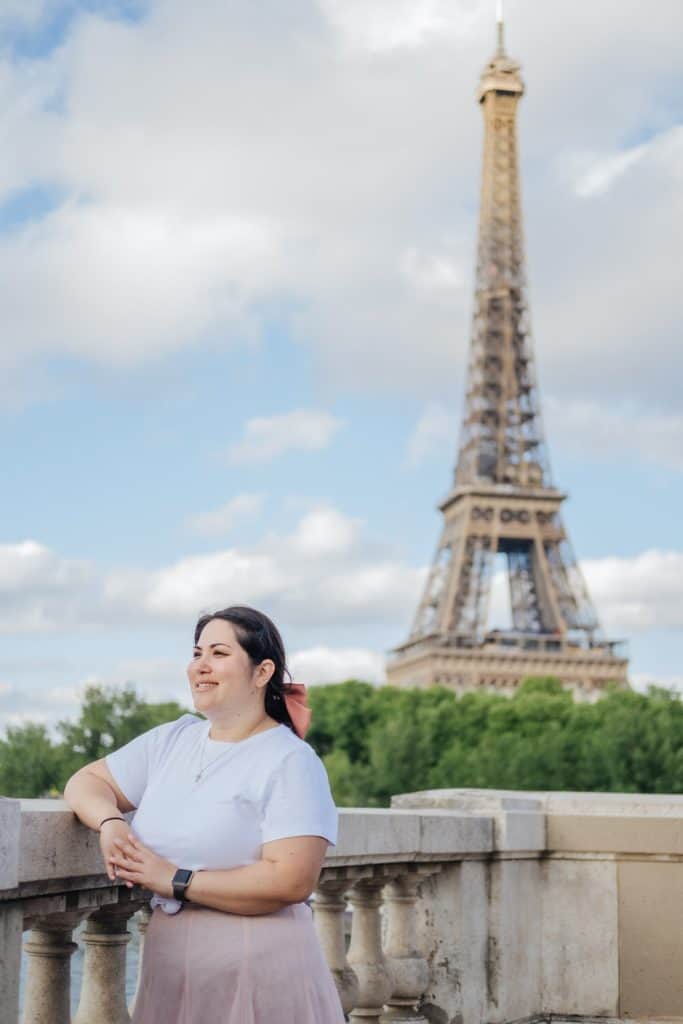 Woman smiling on a bridge with the Eiffel Tower behind her.