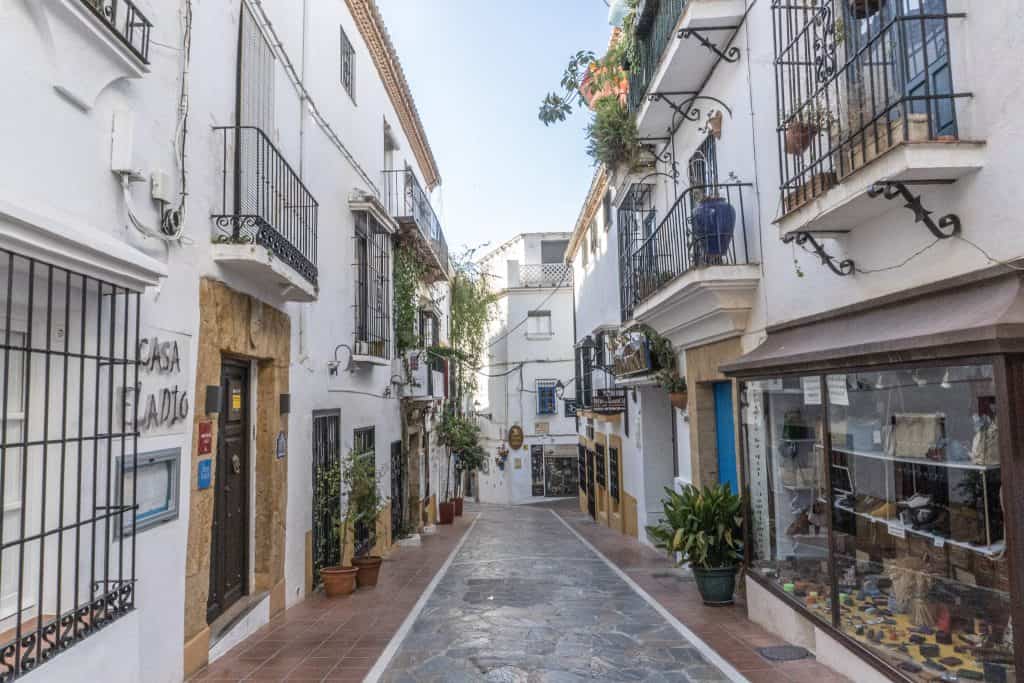 Empty narrow street lined by white shops.