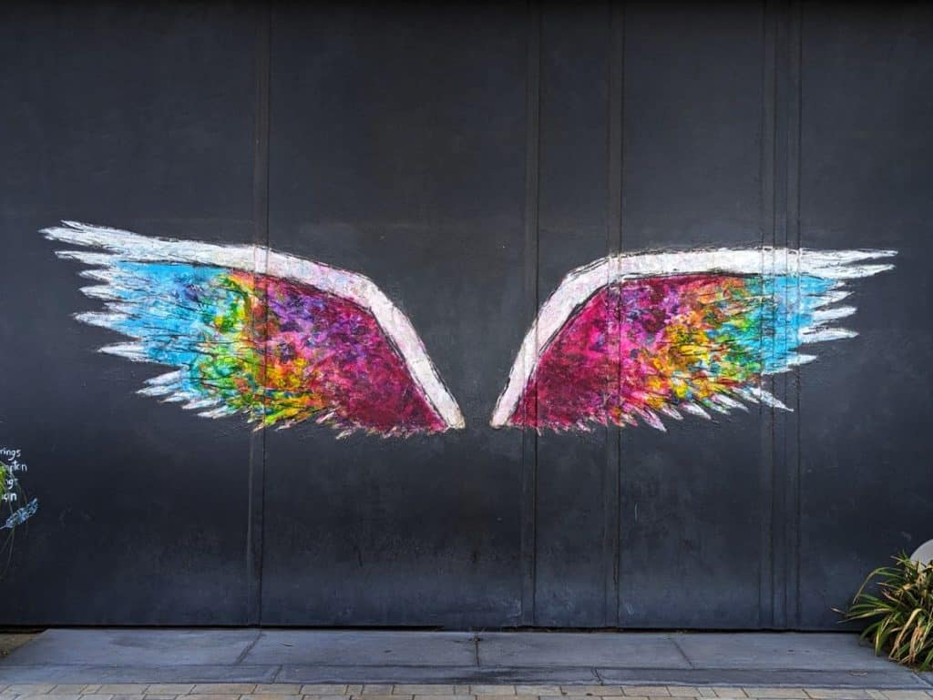 A black wall with a mural of brightly colored wings on it.