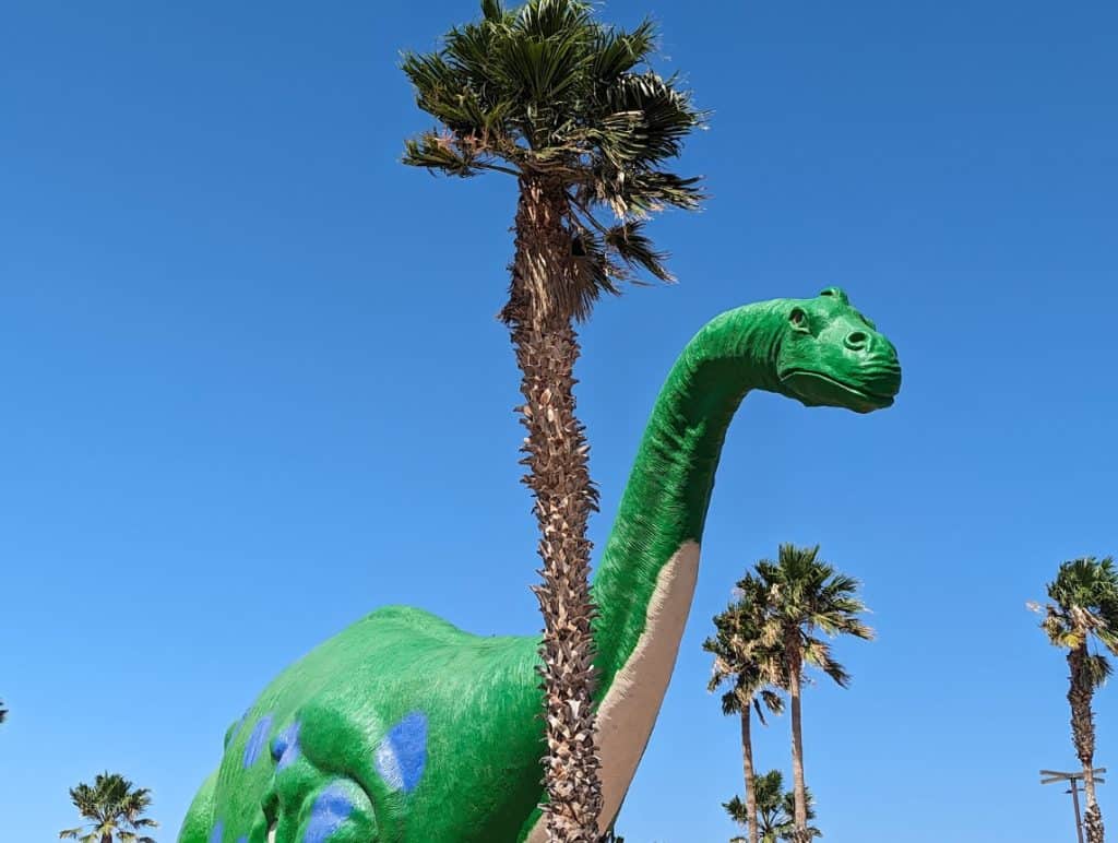A massive green dinosaur statue surrounded by palm trees in Palm Springs.