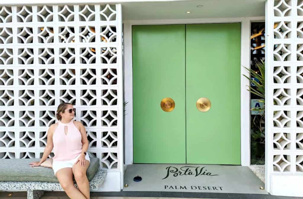 A woman sitting in front of a white wall with a green door next to her.