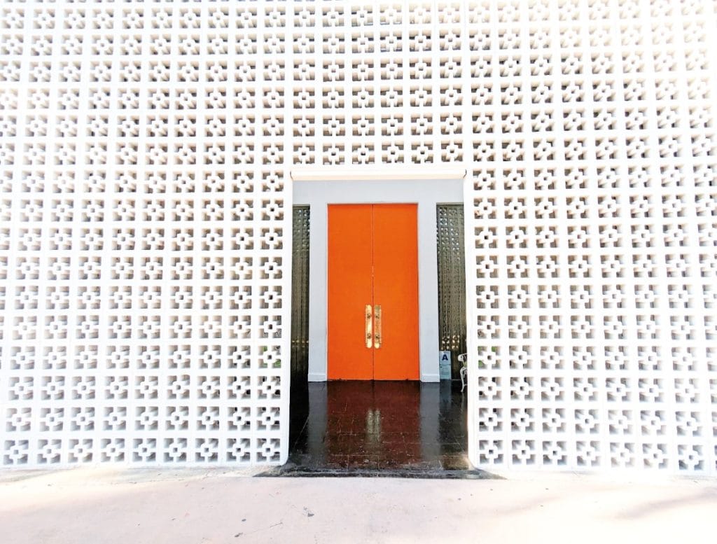 A white wall with a bright red door leading into the Parker Palm Springs Hotel