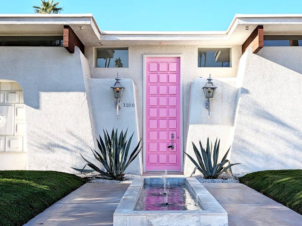 A bright pink door on a home with a small rectangular fountain in front of it.