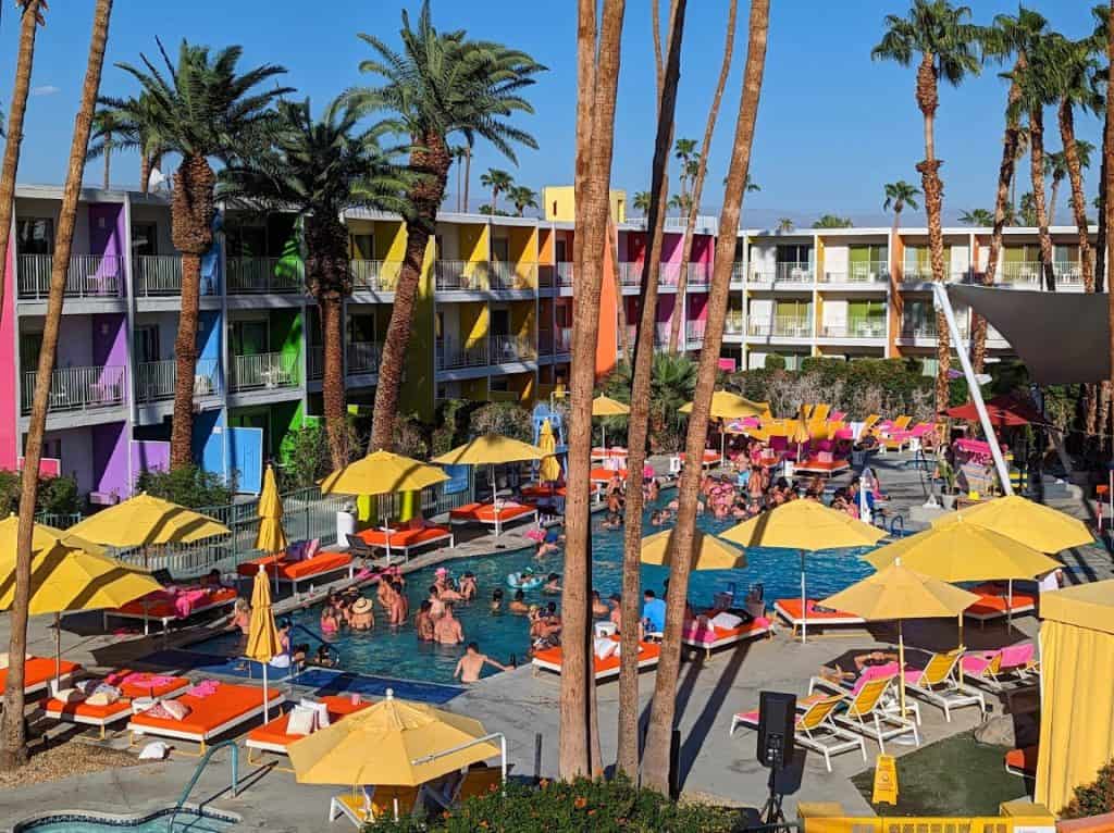 A crowded pool area with yellow umbrellas and the brightly colored walls of the Saguaro Hotel in Palm Spring behind it.