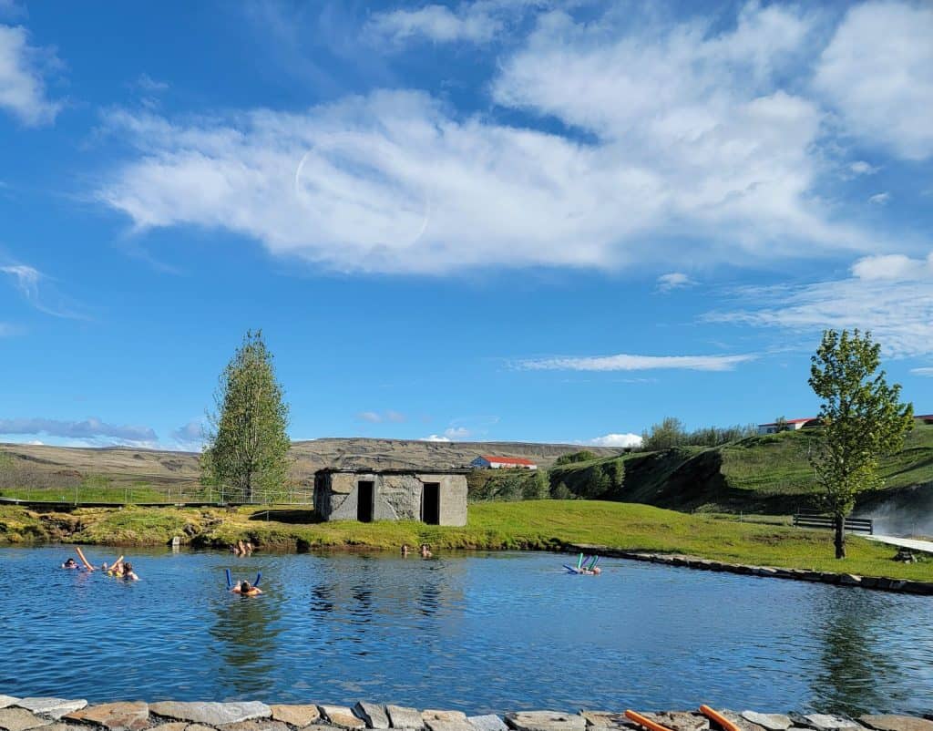 A lagoon in Iceland called the Secret Lagoon surrounded by a green hilly area. 