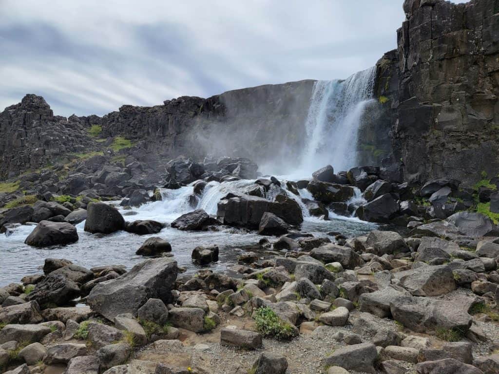 A waterfall flowing over a cliff into a rocky river in Thingvellir National Park in Iceland. 