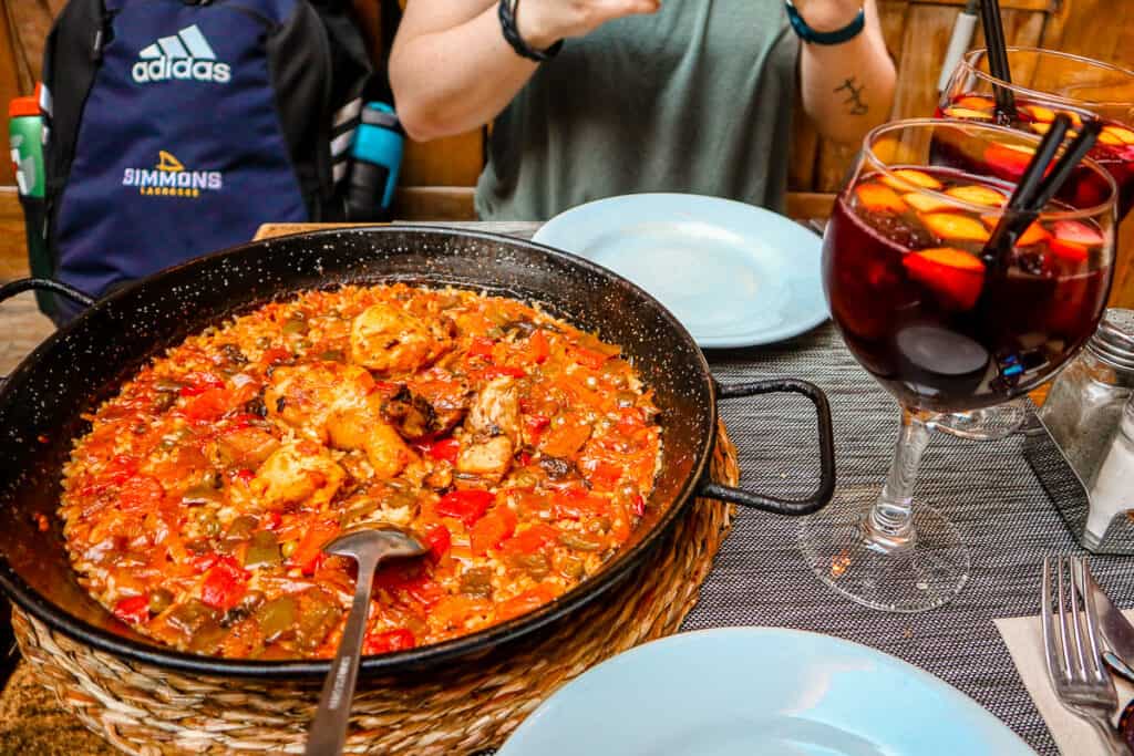A table with a large bowl of Paella and two glasses of sangria on it. 