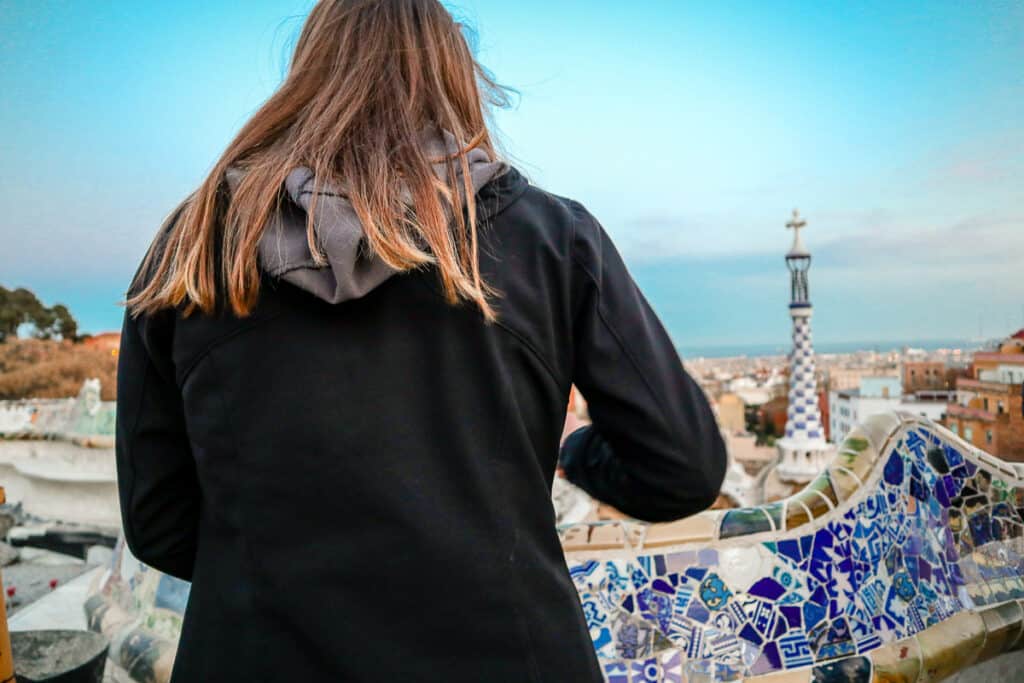 The back of a woman as she stands at a mosaic wall overlooking a city. 