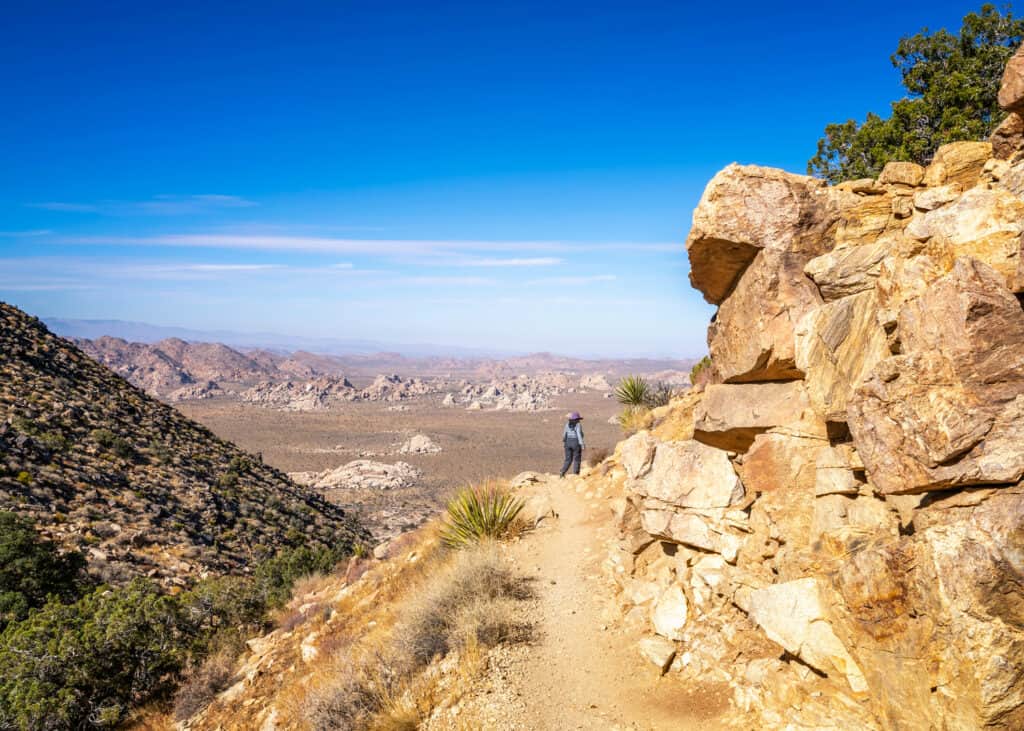 A woman walking along a narrow hiking path. 