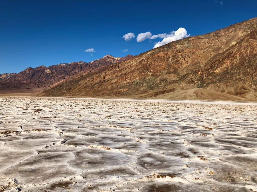 The vast salt flats of Badwater Basin stretching towards the colorful mountain ranges under a blue sky in Death Valley National Park