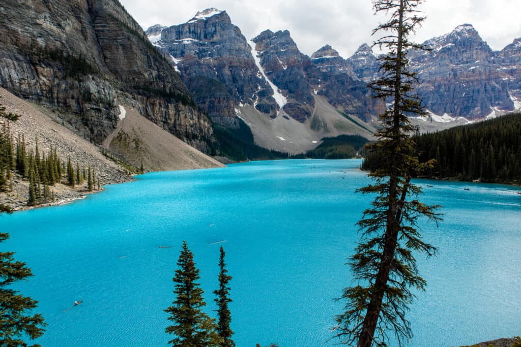 Bright blue water surrounded by snow-capped mountains and lush green trees