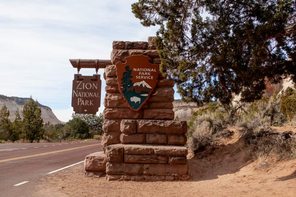 Stone formation with 2 signs that read Zion national park and national park service