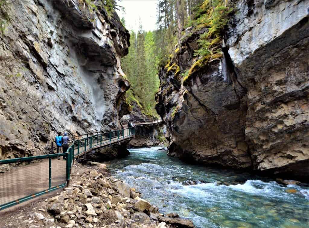 HIkers walking along bridge parallel to fast stream between rocky cliffs