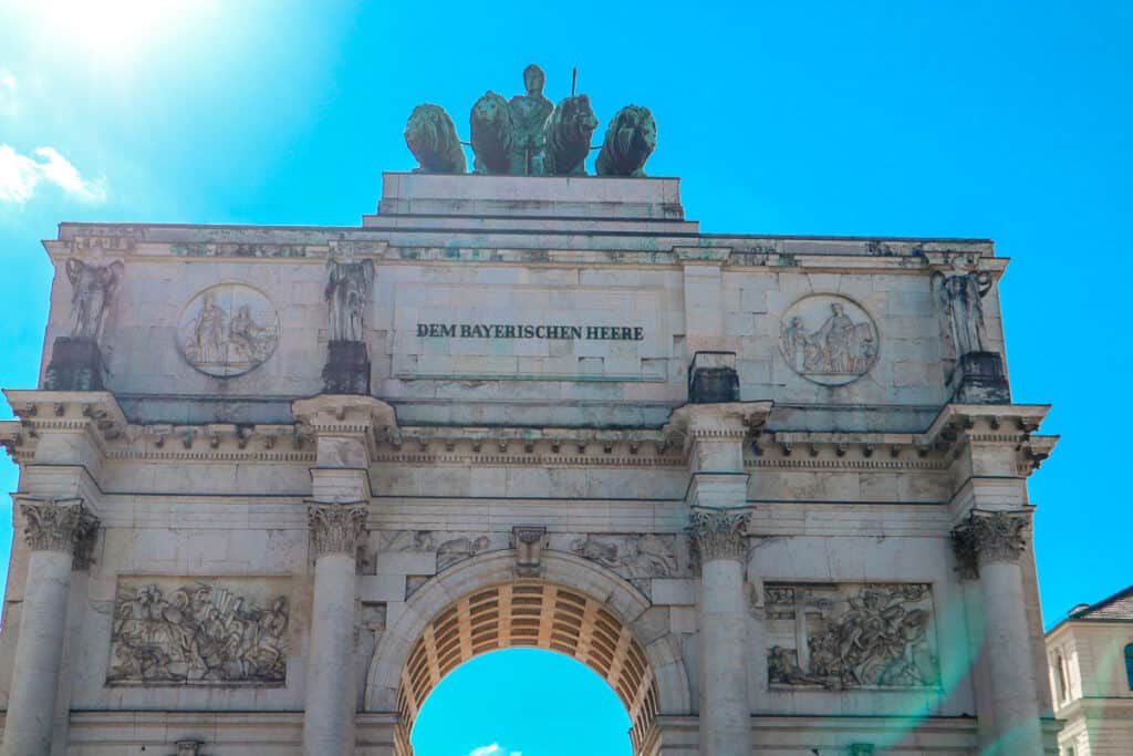 The Siegestor, a triumphal arch in Munich, bathed in sunlight with intricate sculptures and bas-reliefs, symbolizing peace and victory.