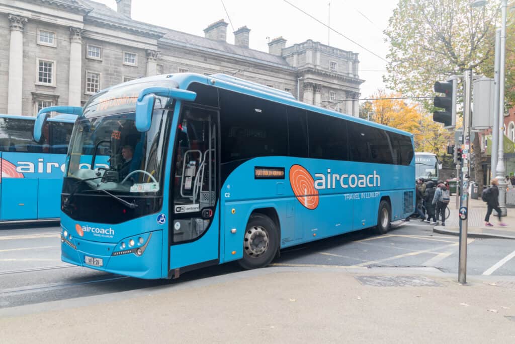 The iconic blue Aircoach bus parked, providing transport services from Dublin city center to the airport, with pedestrians walking by.