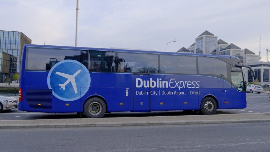 A Dublin Express coach, colored in bright blue, parked on a city street, offering direct airport transport services.