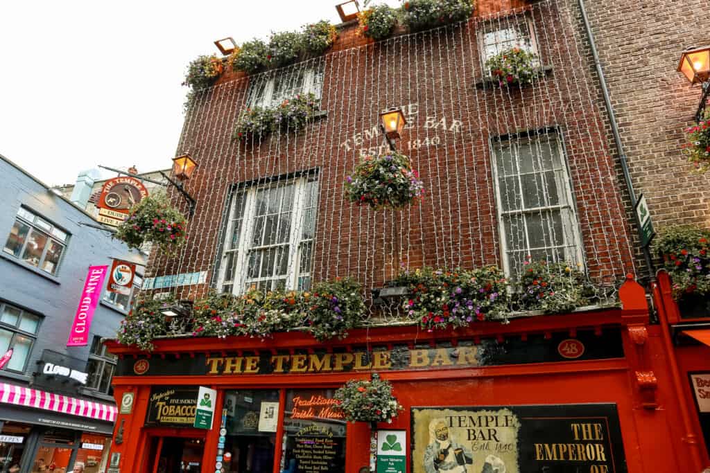 The famous Temple Bar in Dublin, its red exterior festooned with lush flower arrangements, renowned for its traditional Irish music and pub atmosphere.